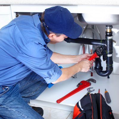 Mature plumber fixing a sink at kitchen