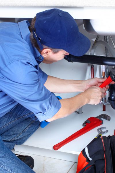 Mature plumber fixing a sink at kitchen