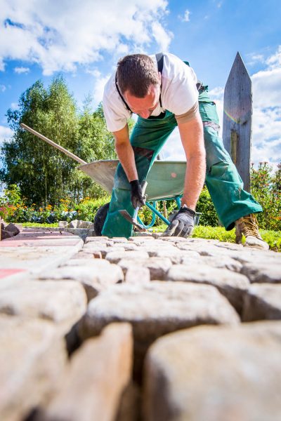 Handwerker verlegt Pflastersteine in einer Gartenanlage