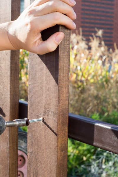 Close up of hand screewing wood plank to metal construction. Building a wooden fence with a drill and screw.