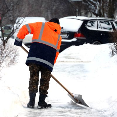 Man worker in orange uniform with a shovel cleaning the street n