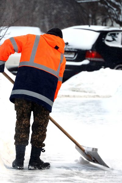 Man worker in orange uniform with a shovel cleaning the street n